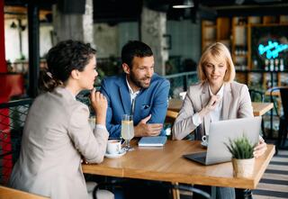 three business professionals sitting at a restaurant table with focused attention on a laptop screen