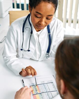 medical doctor sitting at desk pointing to a document using a pen held in their right hand