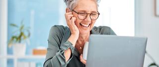 happy senior businesswoman holding a coffee cup looking at a laptop screen